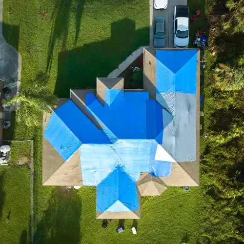 Aerial view of a storm-damaged roof covered with emergency tarps